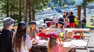 Children enjoy an outdoor crafting session in nature, accompanied by the sound of a nearby river and the picturesque Alpine landscape at Hotel Bella Vista South Tyrol.