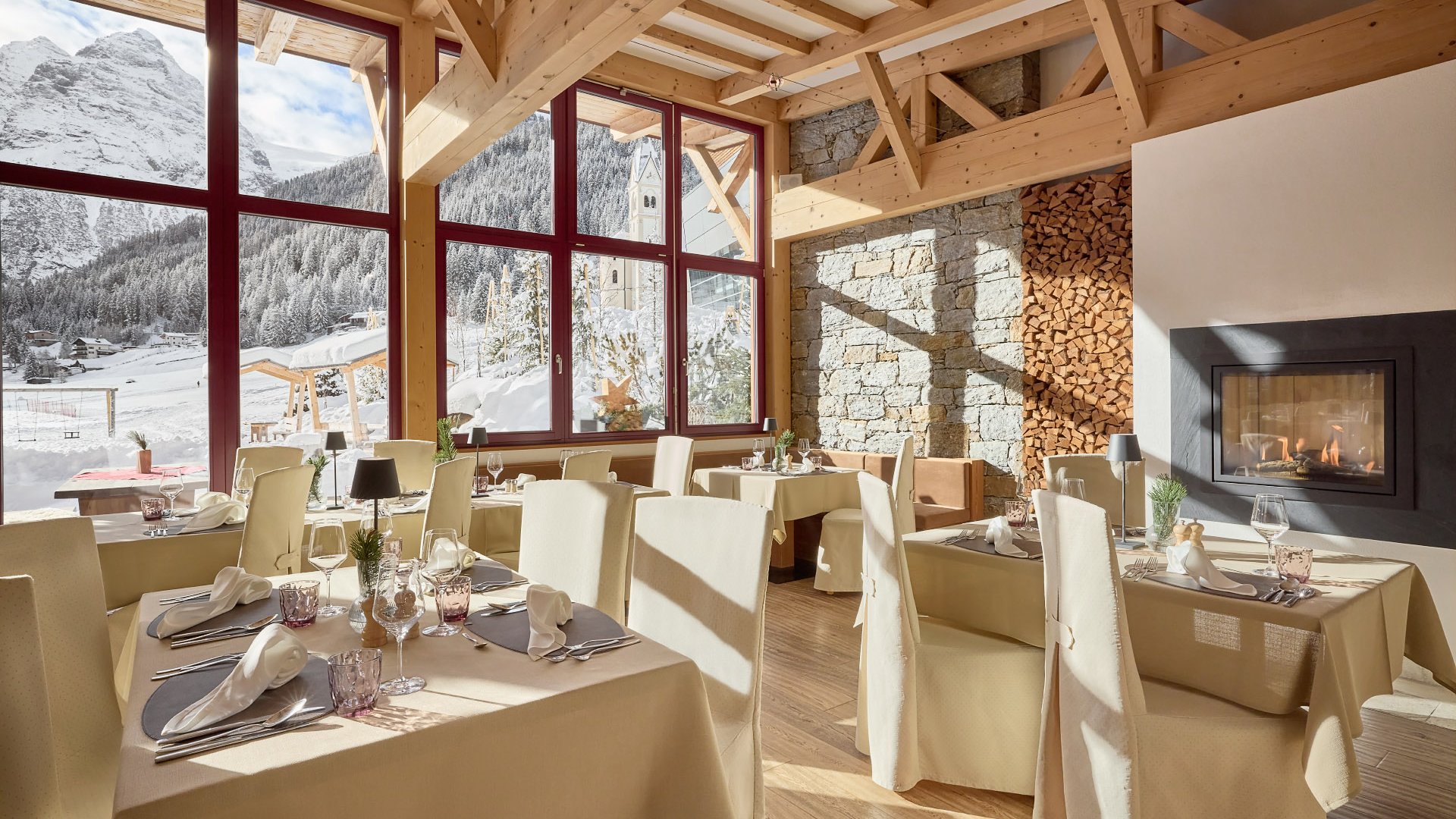 Restaurantbereich im Hotel Bella Vista mit traditioneller Holzbalkenarchitektur und elegantem Interieur, große Fenster bieten eine Aussicht auf die Südtiroler Alpenlandschaft.